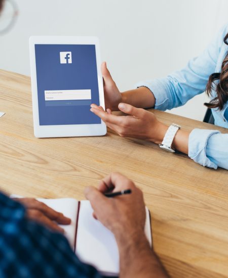 partial view of businesswoman with tablet with facebook logo and colleague with notebook taking part partial view of businesswoman with tablet with facebook logo and colleague with notebook taking part